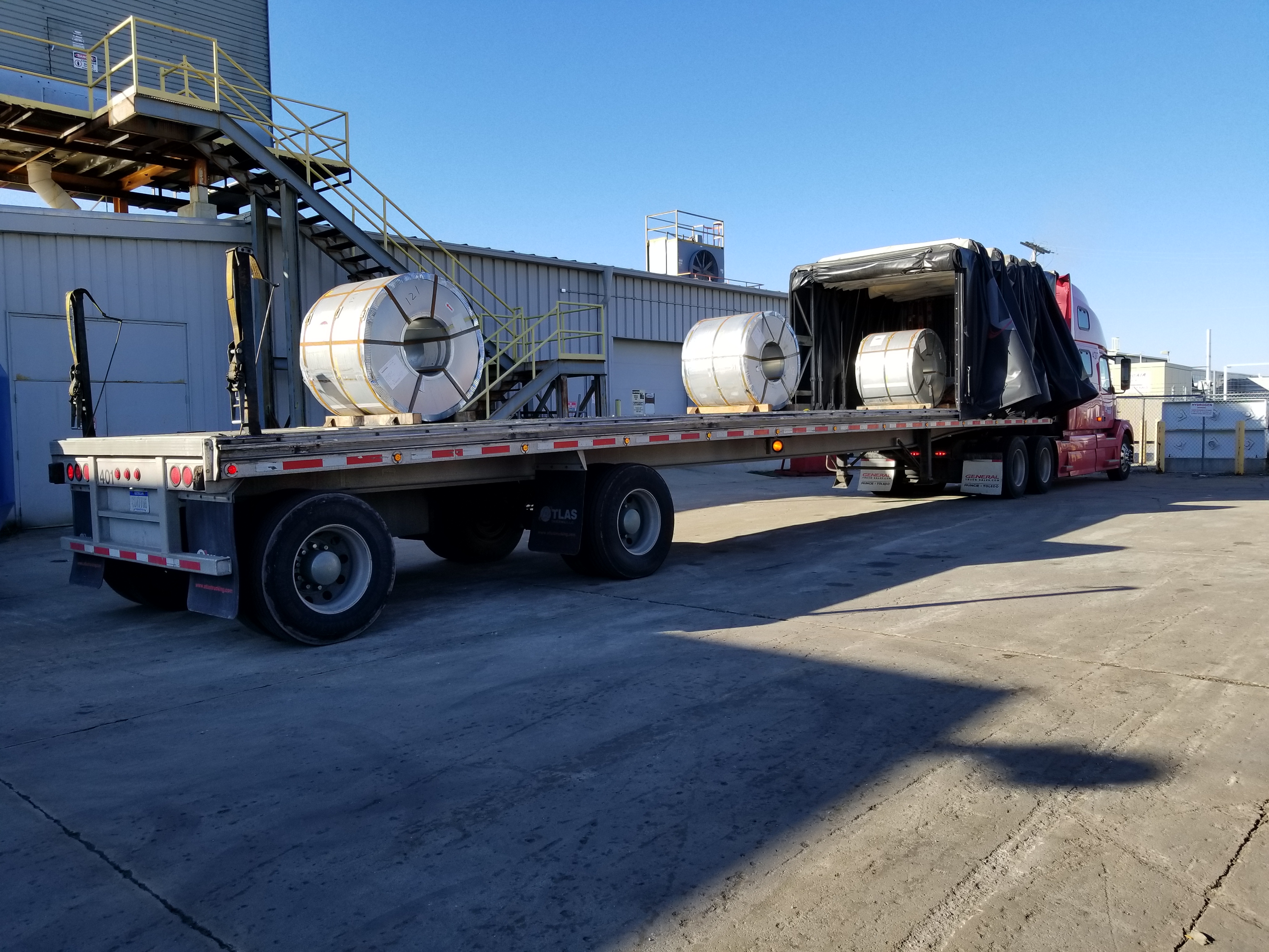 Flatbed truck loaded with three large, circular items.